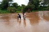 Three men stand knee-deep in brown coloured water as they inspect a water monitoring station, with lush greenery lining the bank behind them thumbnail